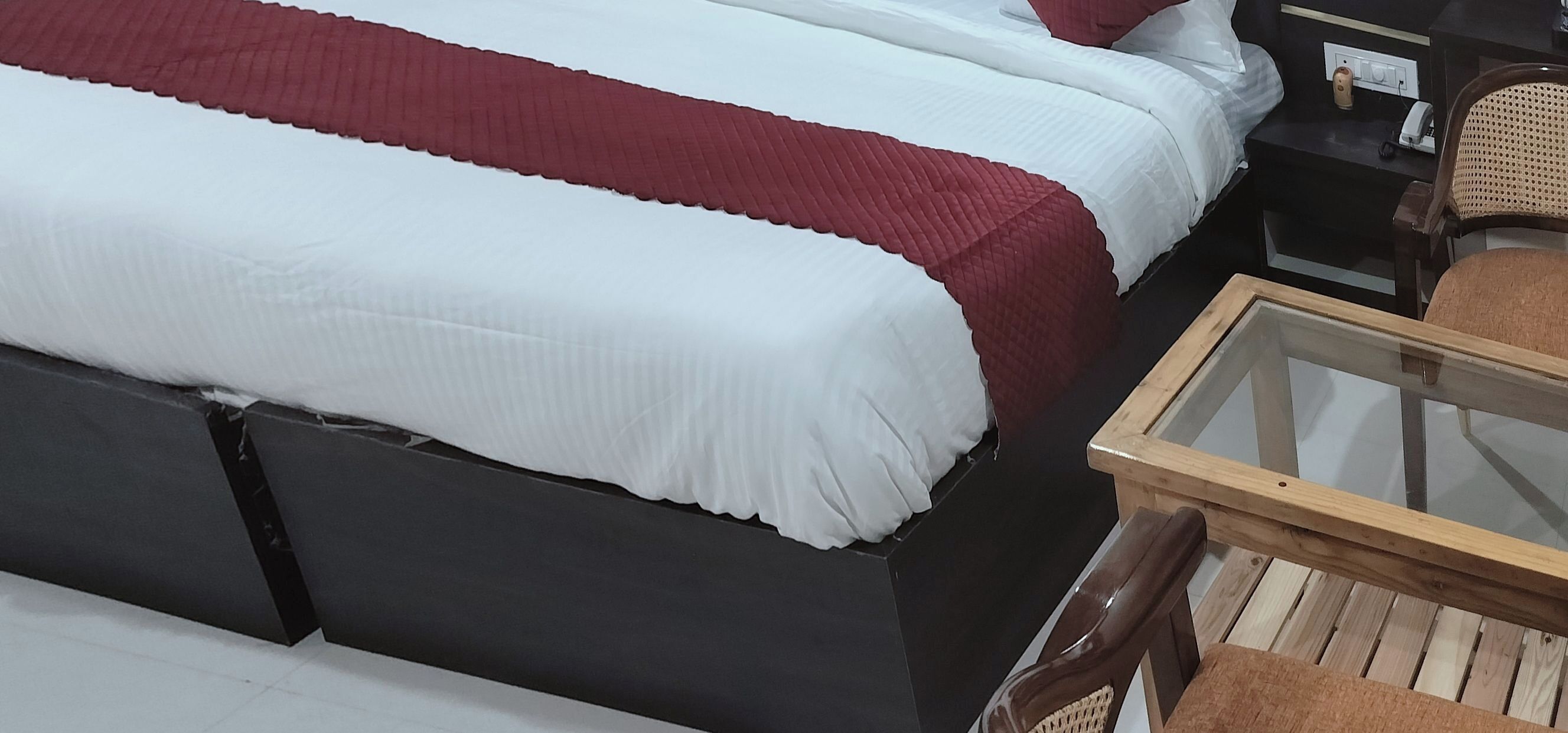 Een slaapkamer met twee bedden, een houten nachtkastje, een glazen bijzettafeltje en een rieten stoel.