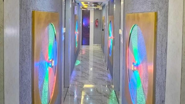 A hallway with a marble floor, curved ceiling lights, and circular light fixtures on the walls. - Hotel Raj Palace (Ahmedabad)