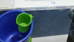 A bathtub with a white interior, blue tiled walls, and a green bucket on a green tray. - Hotel Raj Palace (Ahmedabad)