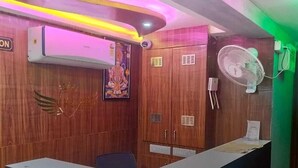 A reception area with a curved reception desk, wooden paneling, a wall-mounted fan, and an air conditioning unit. - Hotel Raj Palace (Ahmedabad)