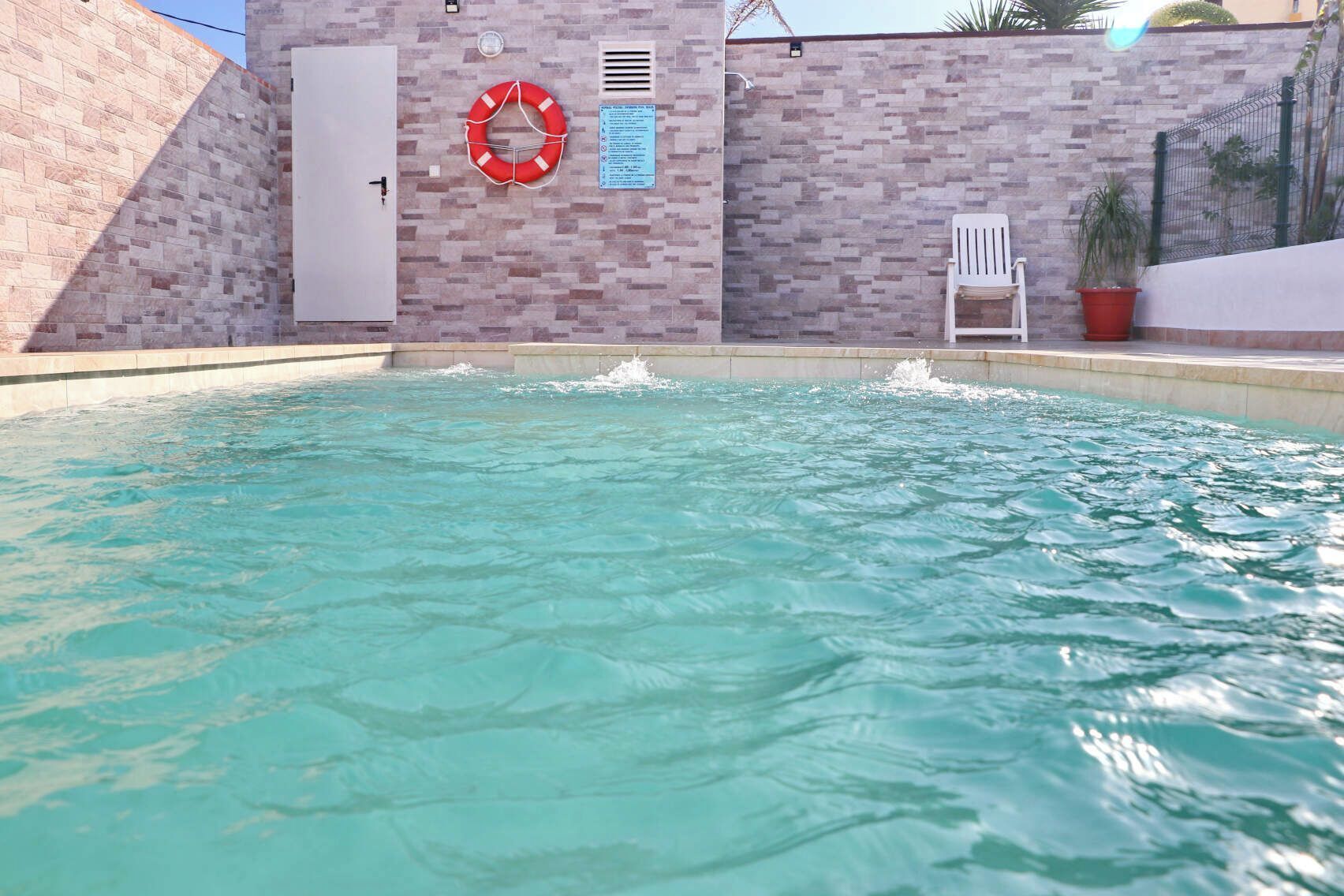 Une piscine à l’eau claire, une bouée de sauvetage et une porte blanche.