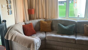 A cozy living room with a sectional sofa, a coffee table, and a fluffy rug. - Seafront Cozy Static Caravan With Sea Vievs (Aberystwyth)