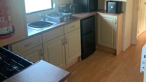 A compact kitchen with a gas stove, microwave, and dishwasher. - Seafront Cozy Static Caravan With Sea Vievs (Aberystwyth)
