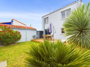 Ein zweistöckiges Haus mit einer Terrasse, einem Grill und einem Esstisch mit Stühlen.