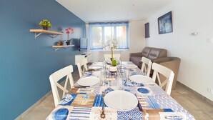 A dining area with a blue and white patterned tablecloth, white chairs, and a window with blue curtains. - House with garden, beach 15 min walk - 6 guests (Les Sables-d´Olonne)