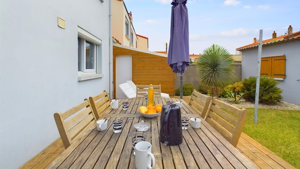 A wooden deck with a table set for breakfast, including cups, a coffee pot, and a bowl of fruit. - House with garden, beach 15 min walk - 6 guests (Les Sables-d´Olonne)