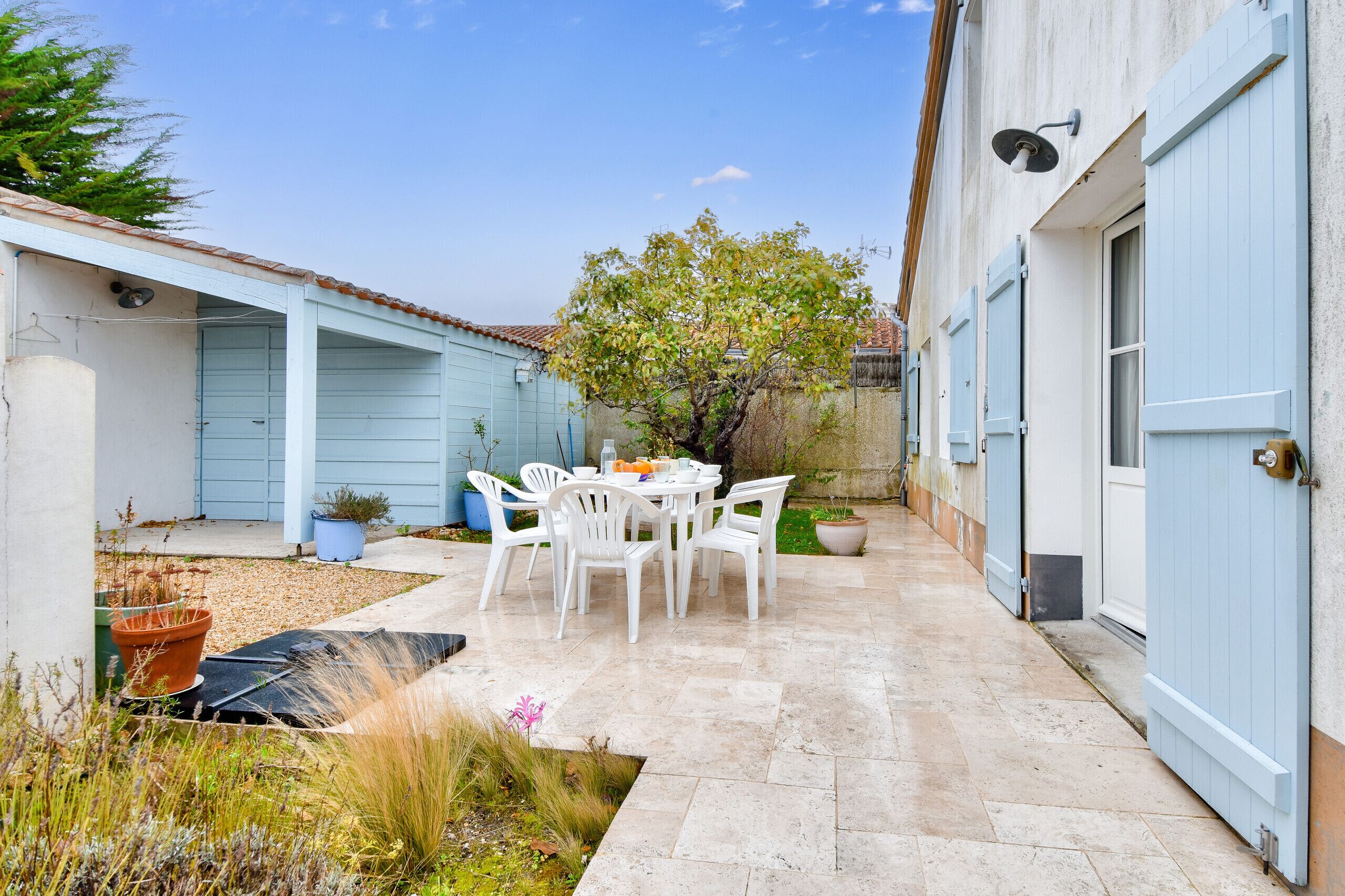 A patio with a table and chairs, a potted plant, and a small garden area.