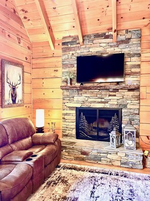 A cozy living room with a stone fireplace, a leather sofa, and a mounted TV.