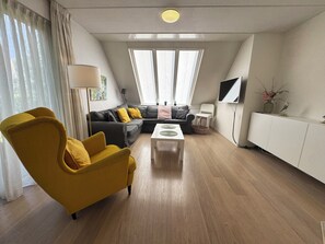 Een moderne woonkamer met een bank, fauteuil, salontafel en een televisie op een wit kastje.