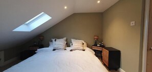 Een slaapkamer met dakraam, een bed met witte beddengoed, twee nachtkastjes met lampen en een klein nachtkastje.