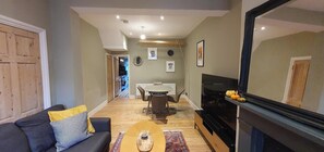 A living room with a sofa, coffee table, TV, fireplace, and dining area. - Cosy & Stylish Stay in Vibrant East Ham (Greater London)