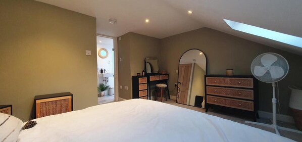 A bedroom with a large bed, a desk, a dresser, a fan, and a skylight.