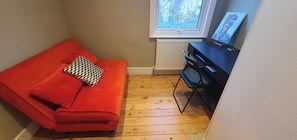 A small room with a red sofa, a black chair, a radiator, and a window with a view of trees. - Cosy & Stylish Stay in Vibrant East Ham (Greater London)