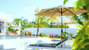 A poolside area with lounge chairs and umbrellas, surrounded by greenery and a white wall. - Aika House - A haven of peace in the heart of Michamvi  (Michamvi Kae.)
