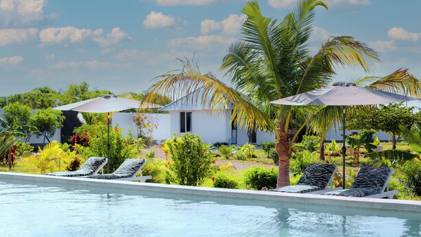 A pool area with lounge chairs and umbrellas, surrounded by greenery and a building in the background. - Aika House - A haven of peace in the heart of Michamvi  (Michamvi Kae.)