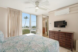 Ein Schlafzimmer mit Bett, Deckenventilator, Fernseher und einem Fenster mit Vorhängen.