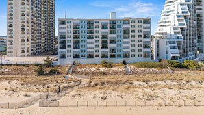 A modern multi-story hotel with balconies and large windows, situated near a sandy beach area. - Oceanfront Condo with Stunning Views, Balcony, & Steps to the Beach! (Ocean City)