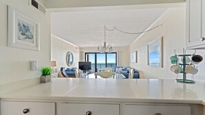 A spacious living area with a large island, a dining table, and a view of the ocean through the windows. - Oceanfront Condo with Stunning Views, Balcony, & Steps to the Beach! (Ocean City)