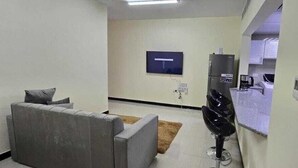 A modern hotel room with a grey sofa, a flat-screen TV mounted on the wall, a minibar, and a small table. - Olaando (Abu Dhabi)