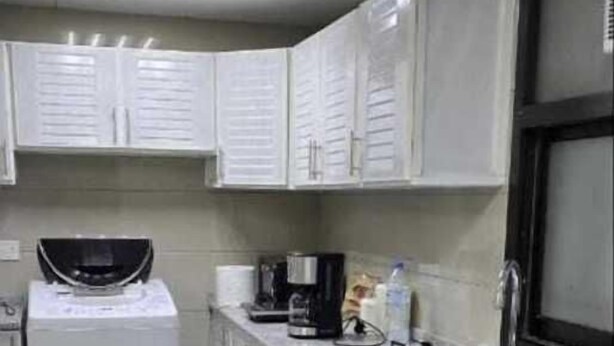 A compact kitchen with white cabinets, a stainless steel sink, a microwave, and a coffee maker. - Olaando (Abu Dhabi)