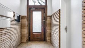 Un couloir étroit aux murs recouverts de lambris en bois, doté d’un sol carrelé et d’une porte en bois avec un panneau en verre dépoli.