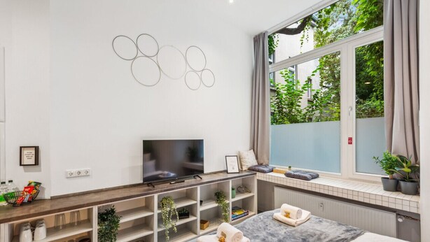 Une chambre moderne équipée d’une télévision, de rangements intégrés, d’une grande fenêtre donnant sur un espace verdoyant et d’un lit avec des serviettes.