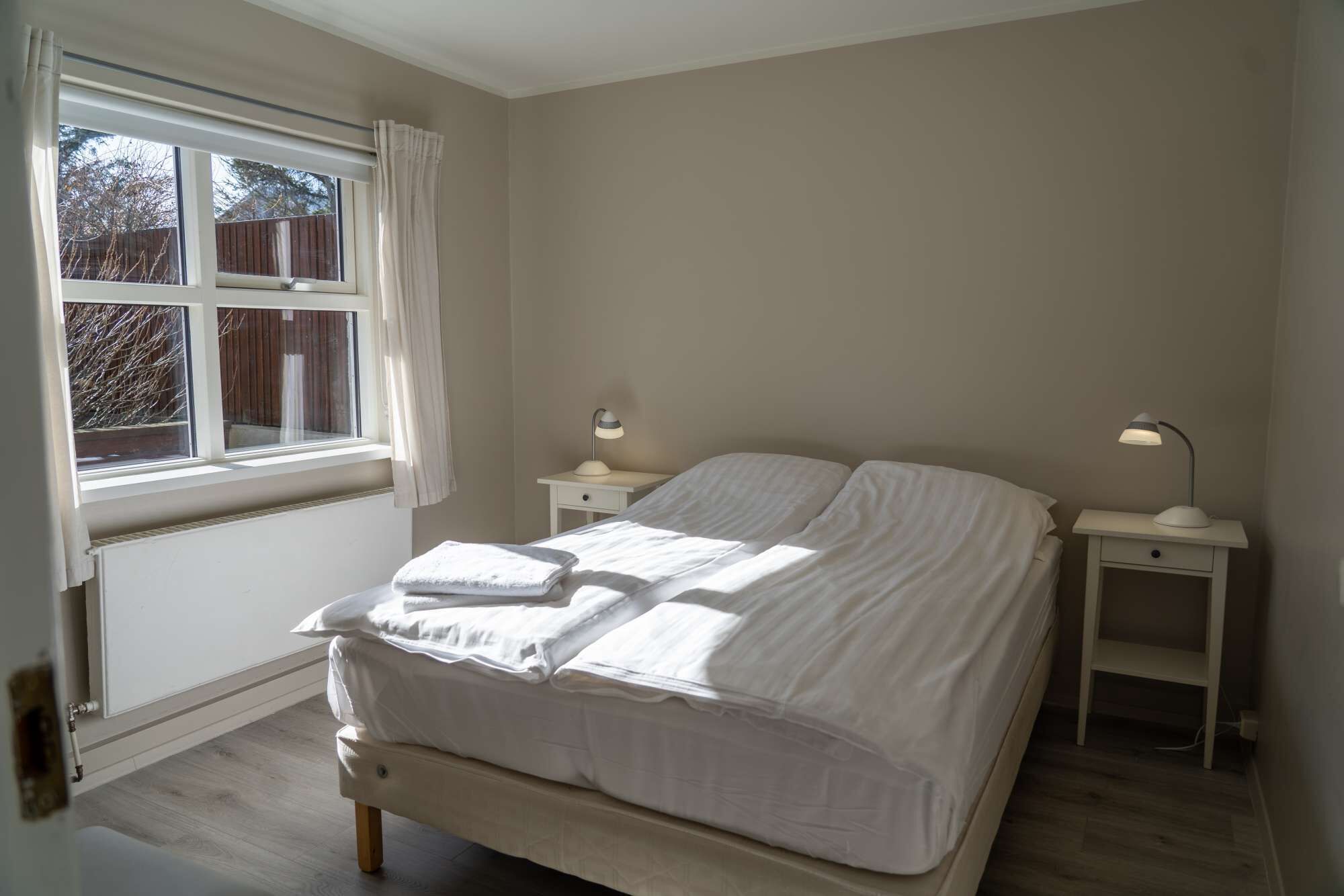 A bedroom with a bed, two bedside tables, and a window with curtains.