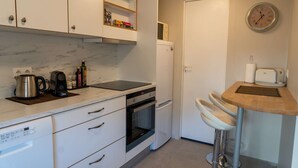 Uma cozinha compacta com armários brancos, forno embutido, cafeteira e um pequeno frigorífico.