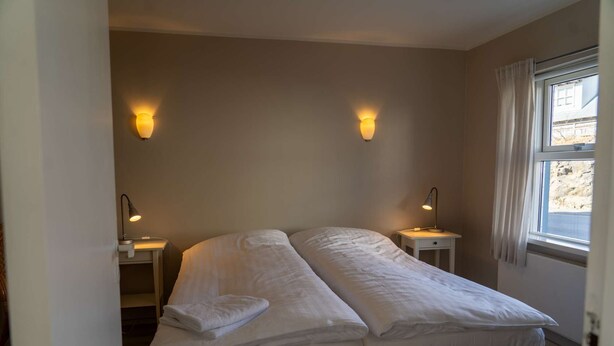 Quarto com cama de casal, duas mesas de cabeceira com luminárias e uma janela com cortinas.