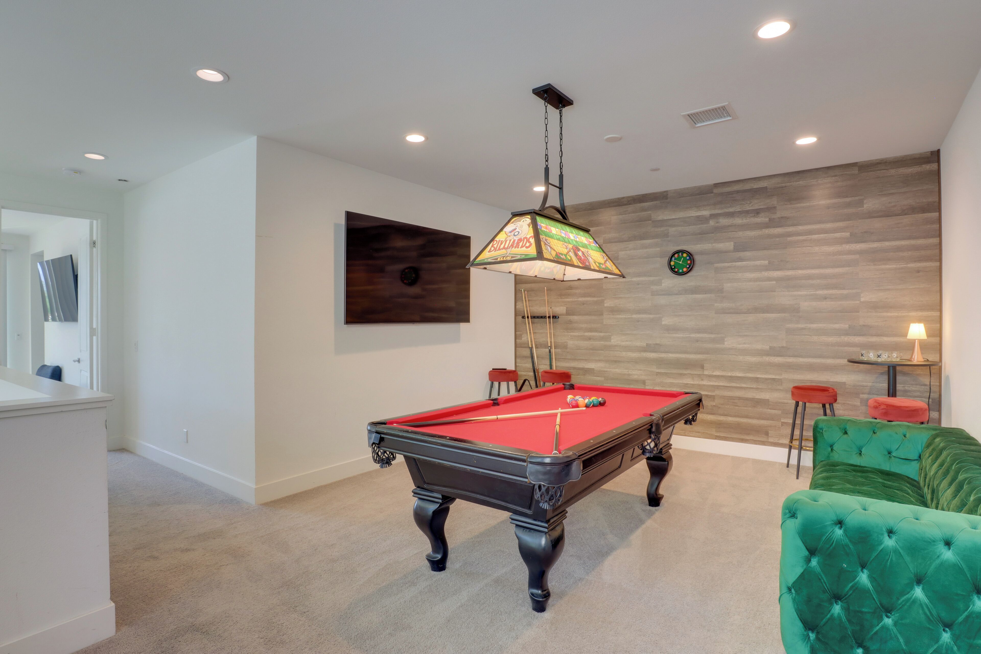 A pool table in a room with a wooden wall, a hanging light fixture, and a green upholstered sofa.