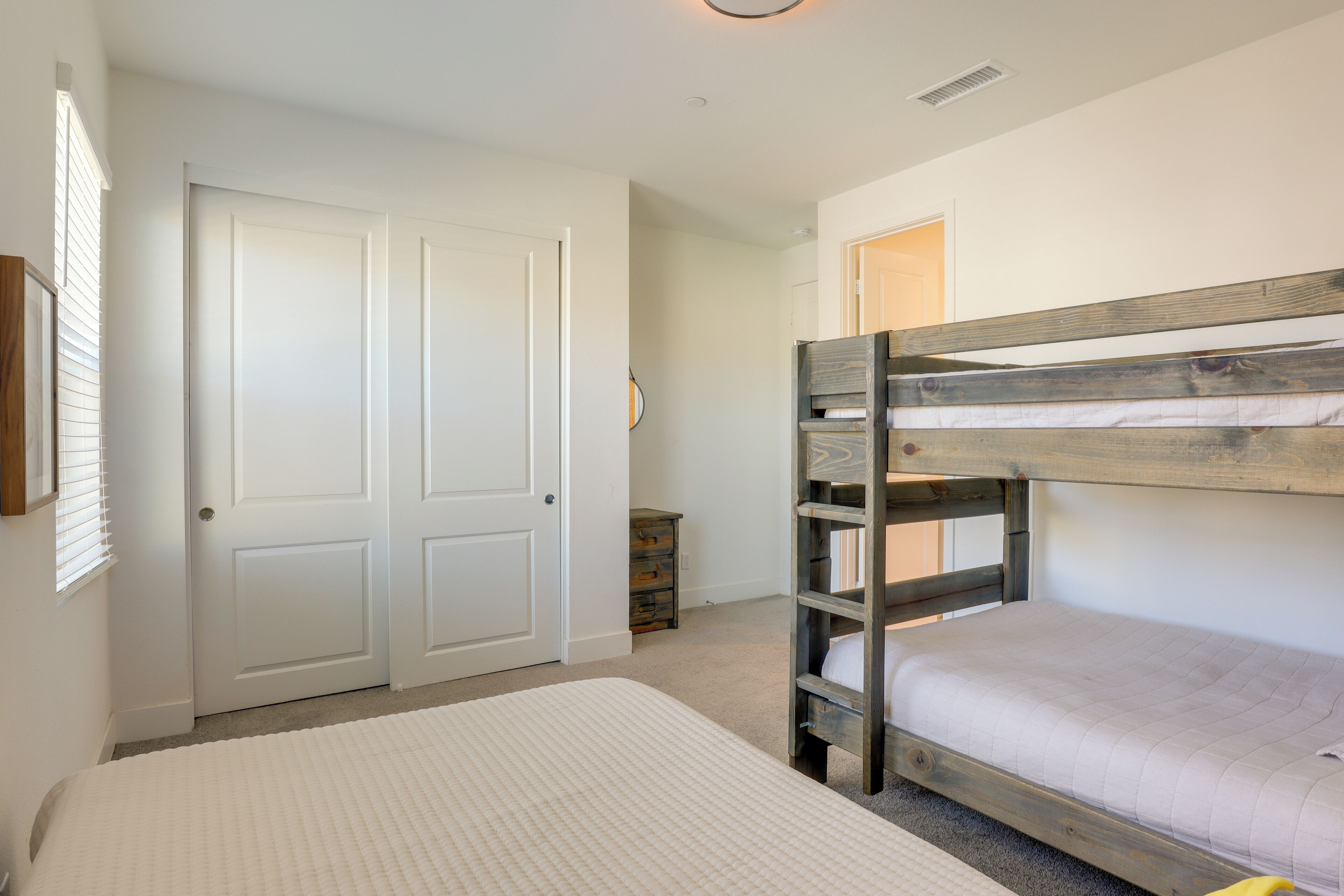 A bedroom with a bunk bed, a large bed, a wardrobe, and a small dresser.
