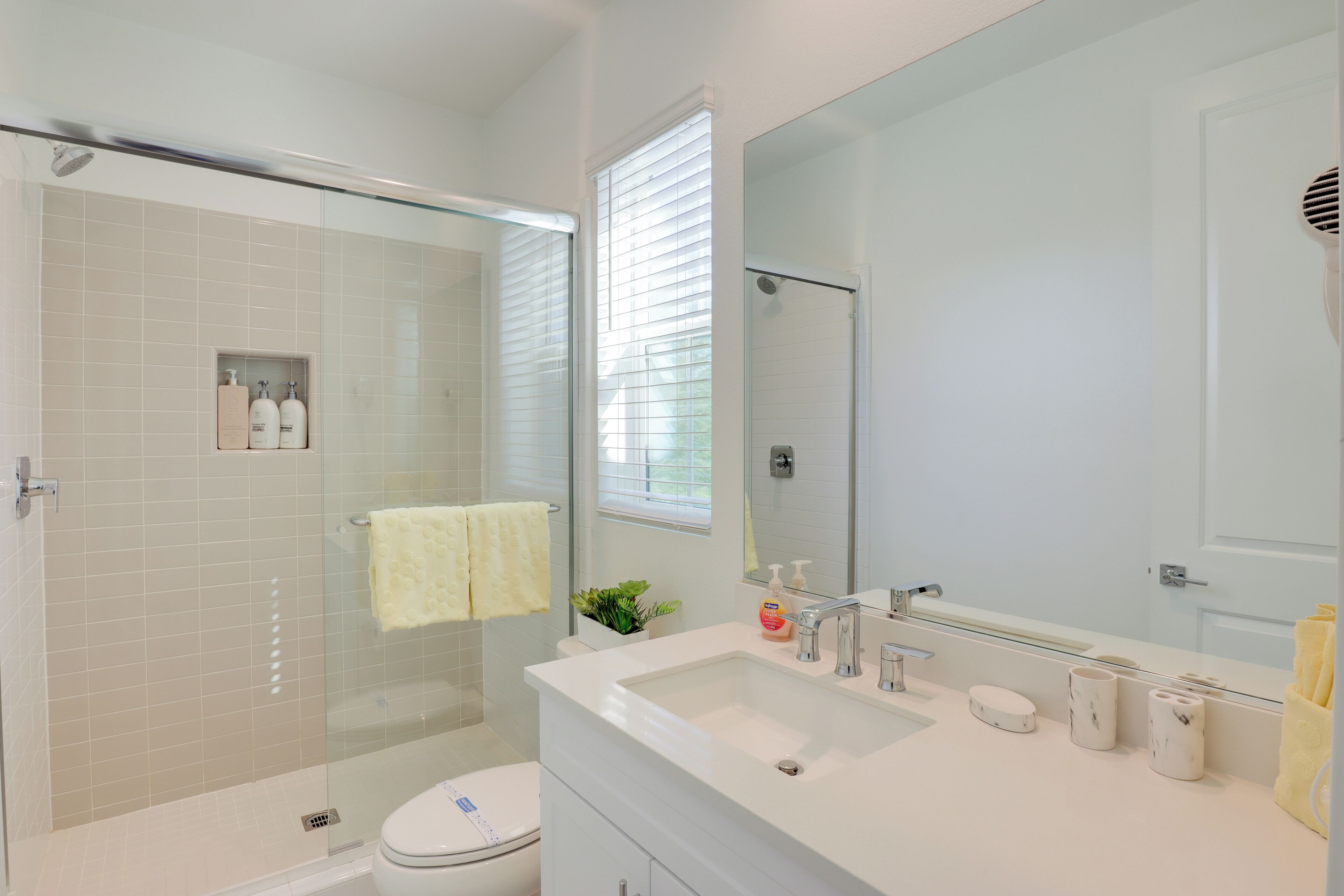 Un baño moderno con ducha de mampara de vidrio, un lavamanos blanco y un espejo grande.