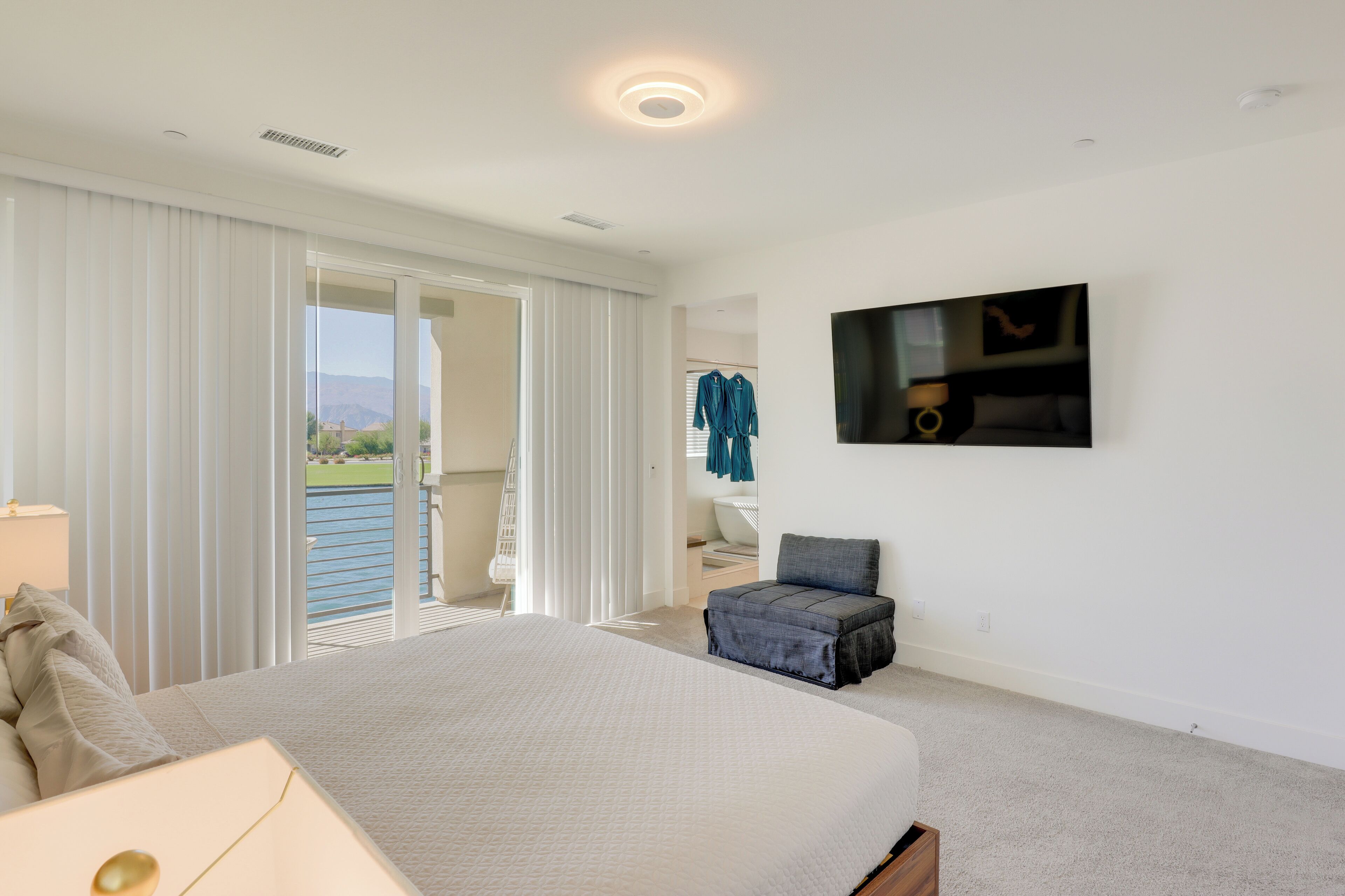 Un dormitorio con una cama grande, un televisor en la pared, una silla y vistas al exterior a través de la ventana.
