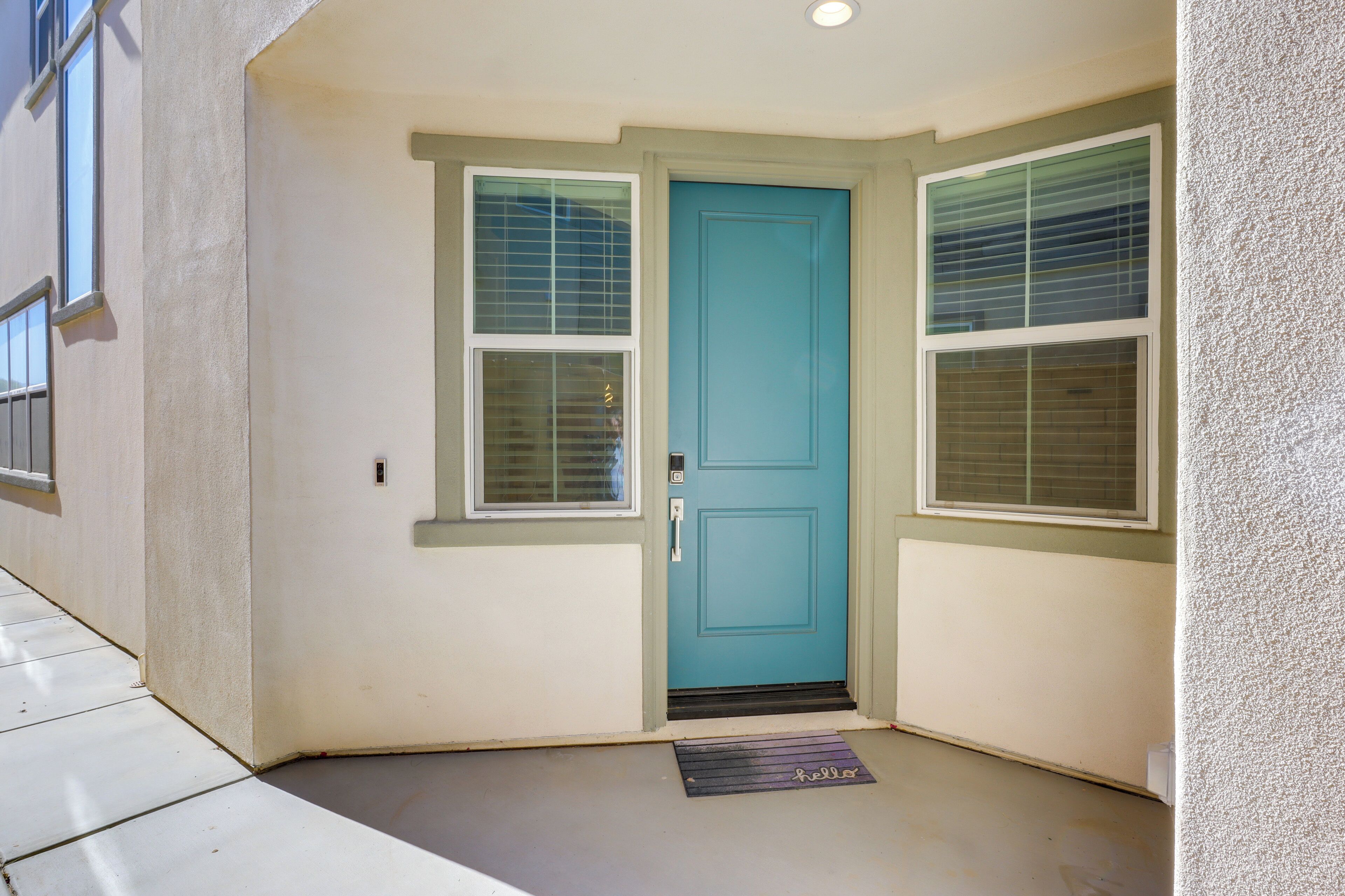 A front door with a blue door and two windows with blinds, a doormat, and a textured wall.