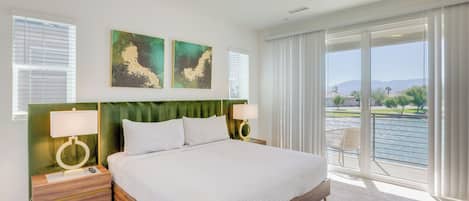 A spacious bedroom with a large bed, two bedside tables with lamps, and a view of a body of water through floor-to-ceiling windows.
