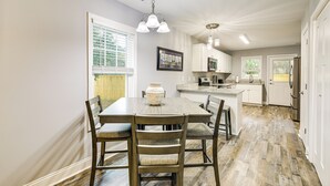 Un coin repas avec une table et des chaises en bois, un vase posé sur la table, et une cuisine en arrière-plan.