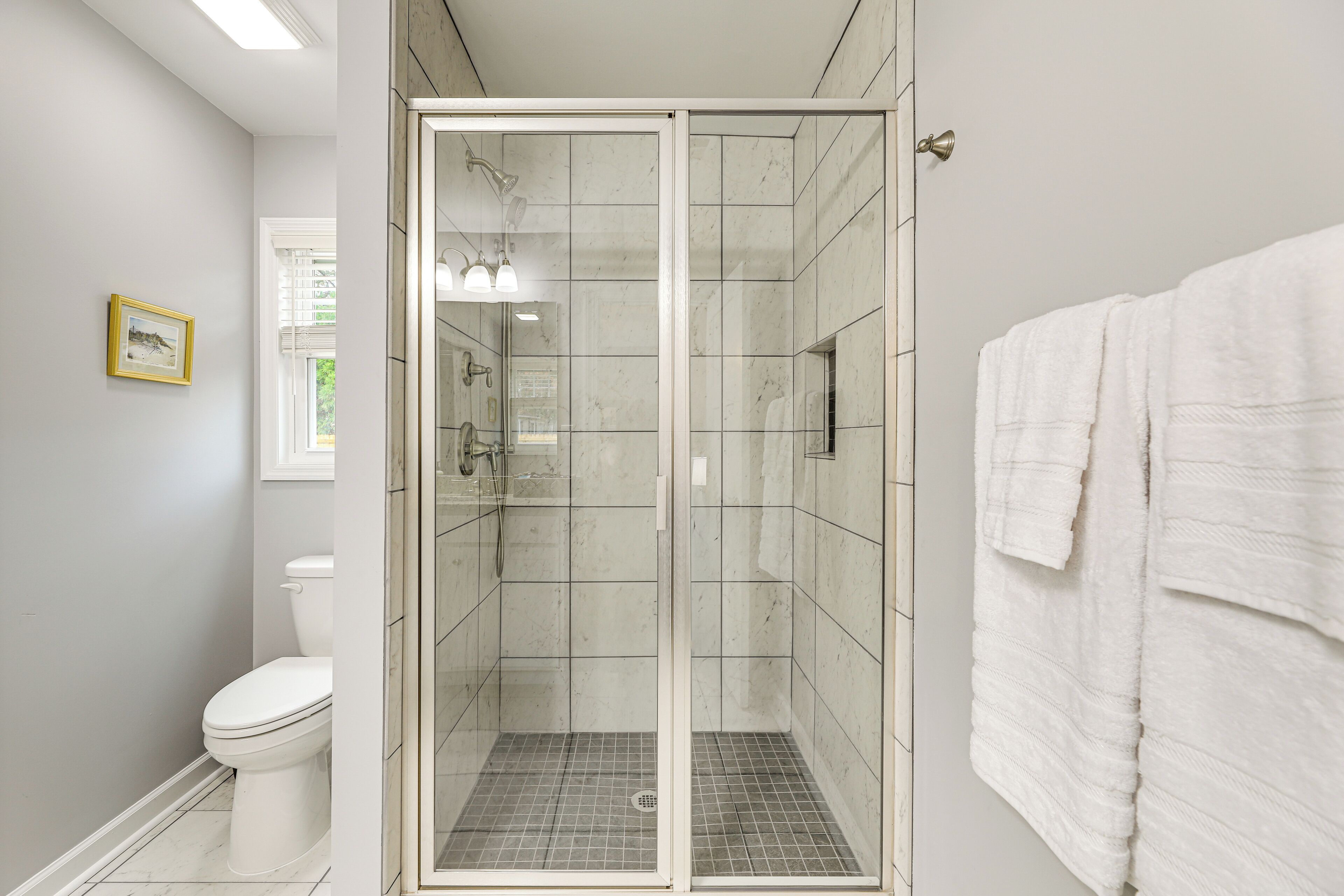 Un baño con ducha acristalada, inodoro y toallero.