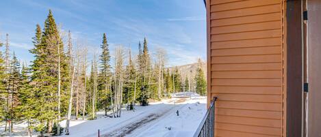 A snowy landscape with a clear sky, a wooden building with a balcony, and a ski slope in the background.