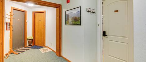 A hallway with wooden doors, a framed picture on the wall, and a potted plant.