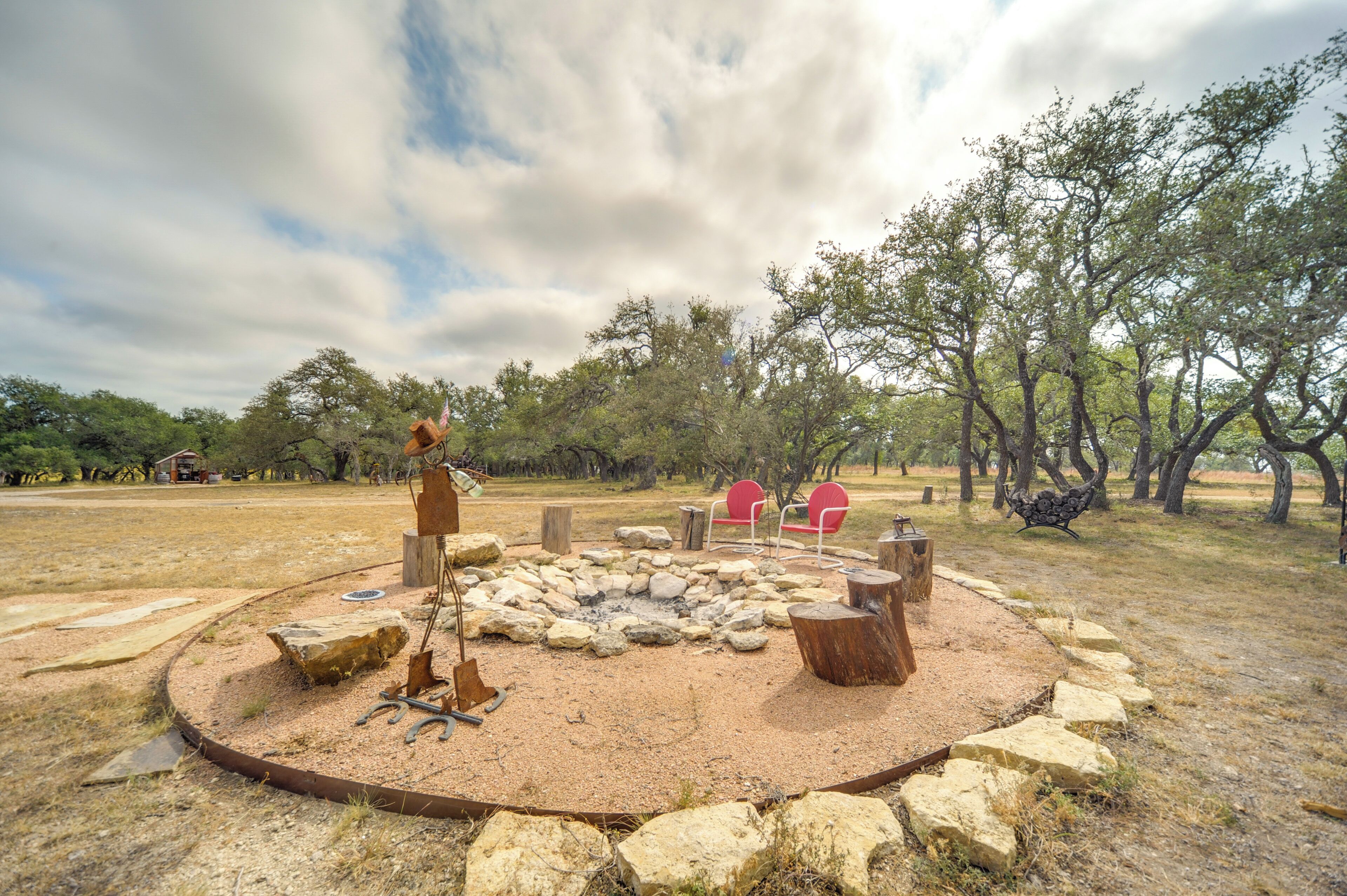 A circular stone fire pit with seating around it, surrounded by a rustic wooden fence and trees.
