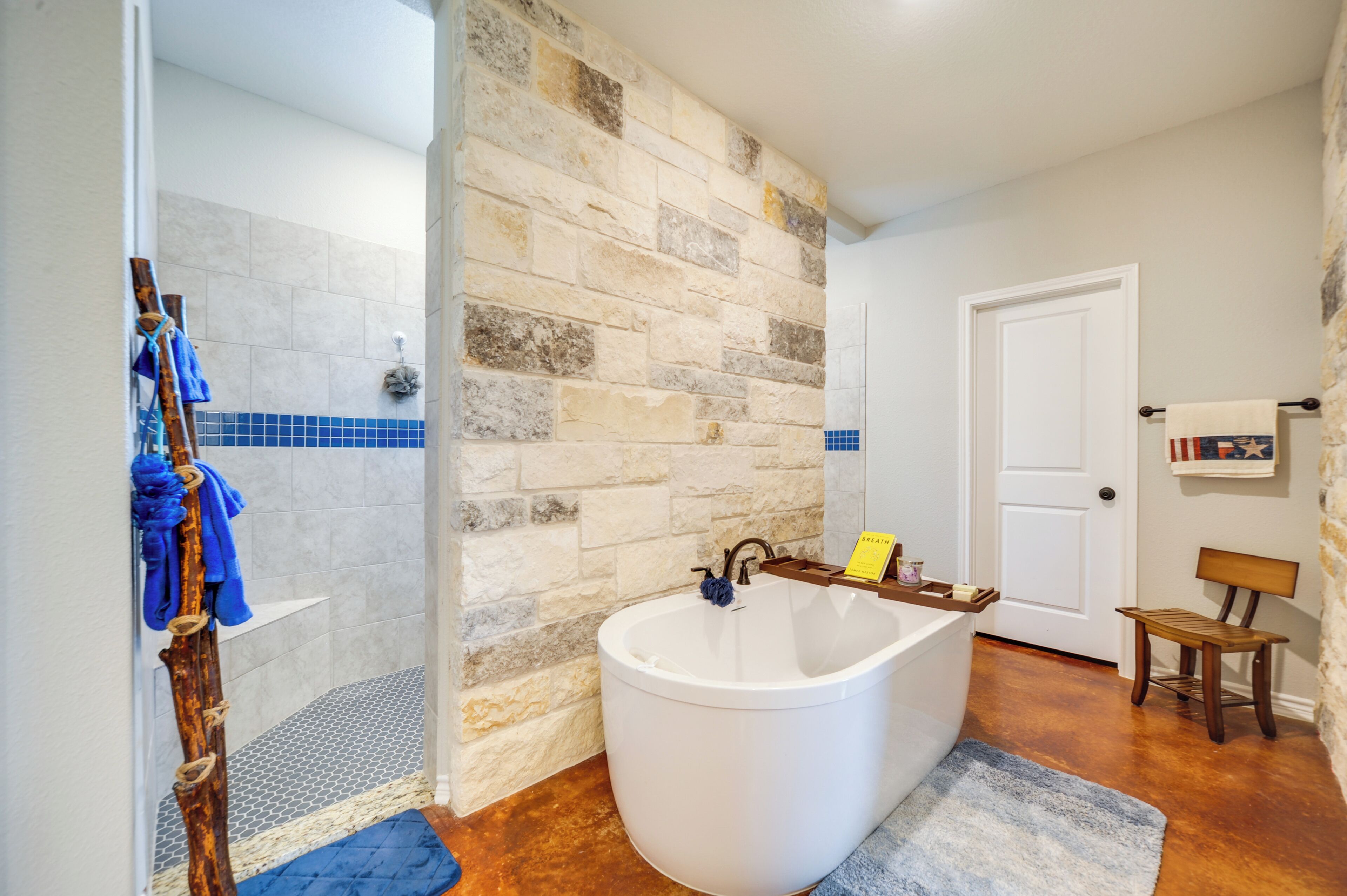Ein Badezimmer mit Steinwand, einer Badewanne, einer Dusche und einer Holzbank.