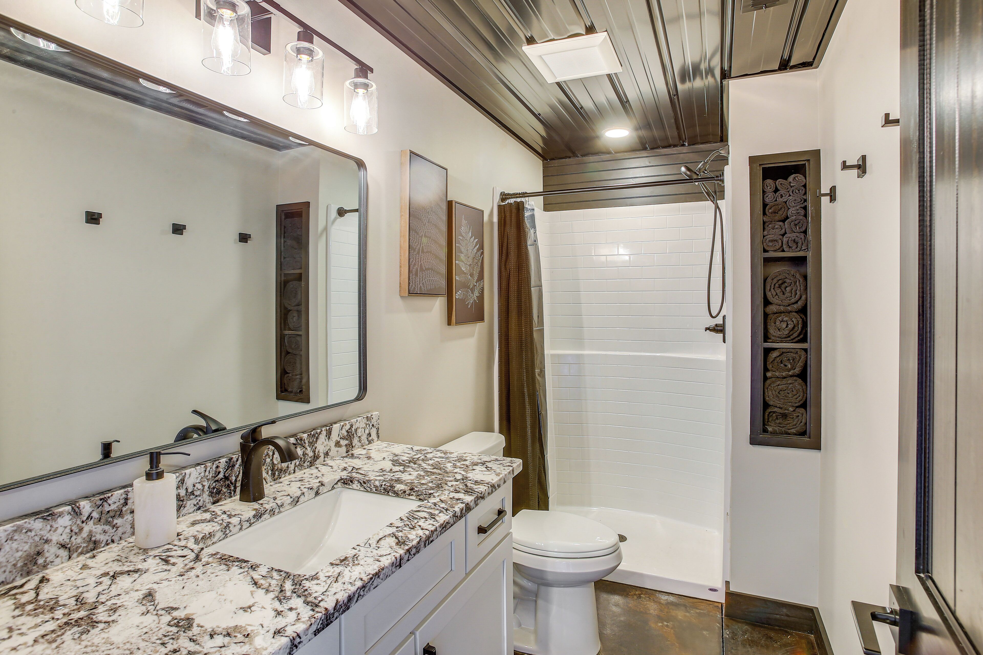A modern bathroom with a large mirror, a marble sink, a toilet, and a walk-in shower.