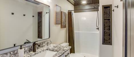 A modern bathroom with a large mirror, a marble sink, a toilet, and a walk-in shower.