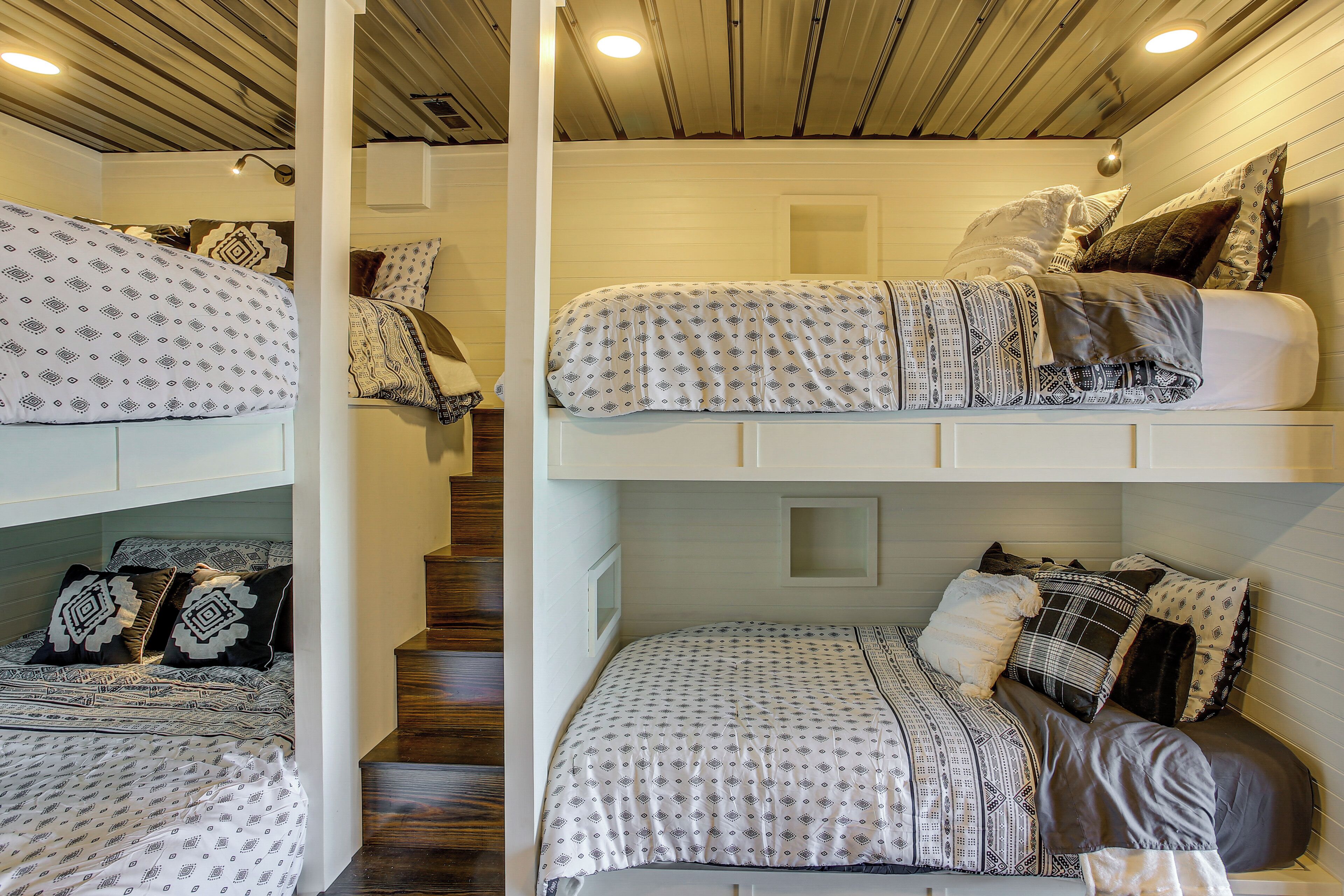 A multi-level bunk bed room with patterned bedding and a wooden ceiling.