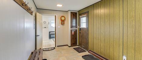 A hallway with a wooden bench, a clock, and a door with a window.