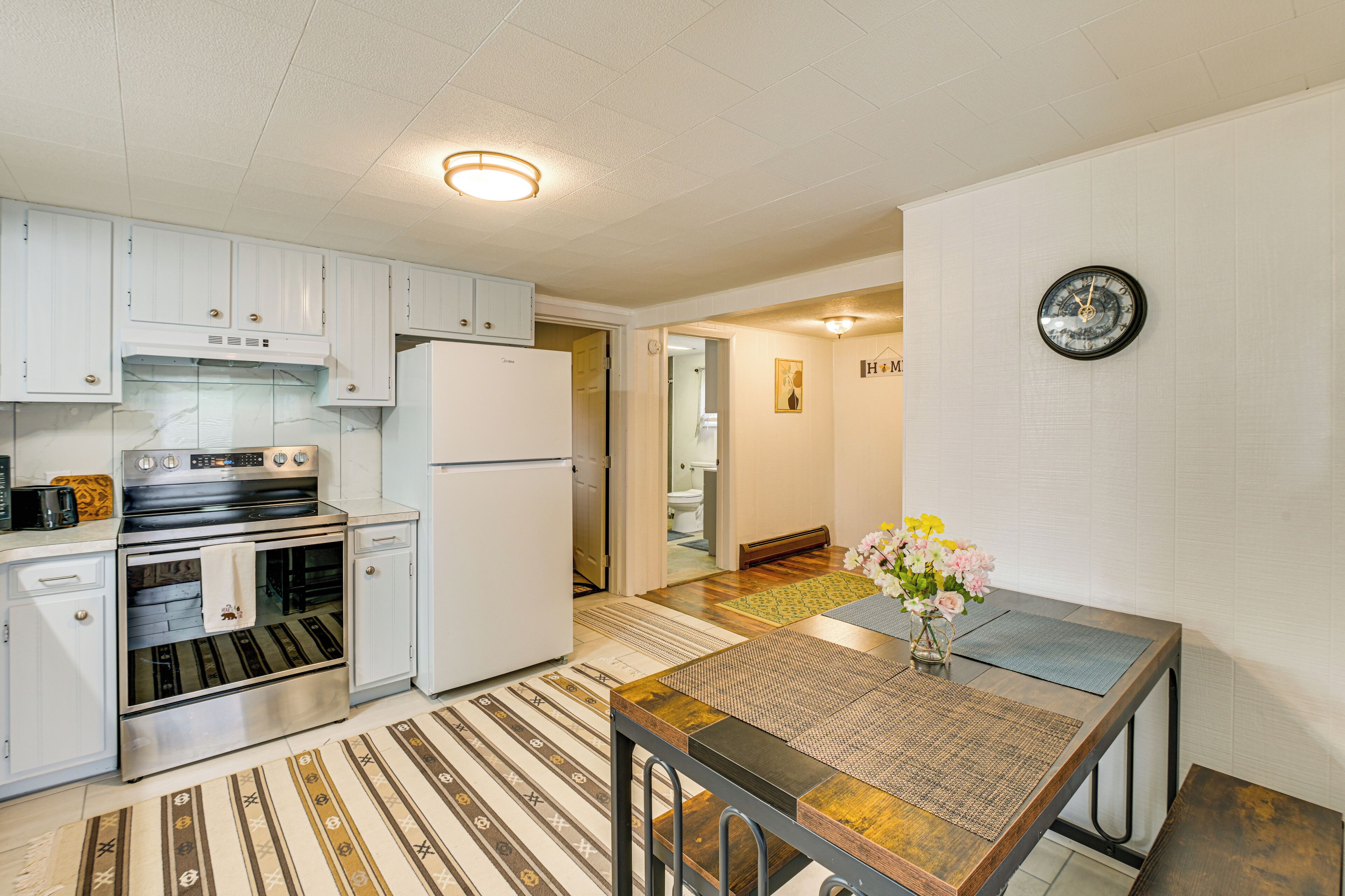 A modern kitchen with white cabinets, stainless steel appliances, and a wooden dining table with a vase of flowers.
