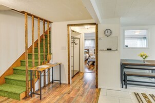 Una escalera con peldaños cubiertos de moqueta verde y barandillas de madera, que conduce a una habitación con piso de madera y una mesa con un jarrón de flores.