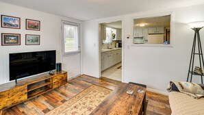 A living room with a flat-screen TV, wooden entertainment unit, and a patterned rug. - Near Skiing & Snowmobiling: Home in Mars Hill! (Mars Hill)