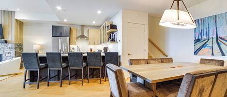 Una cocina moderna con una isla central, sillas oscuras y una mesa de comedor de madera.