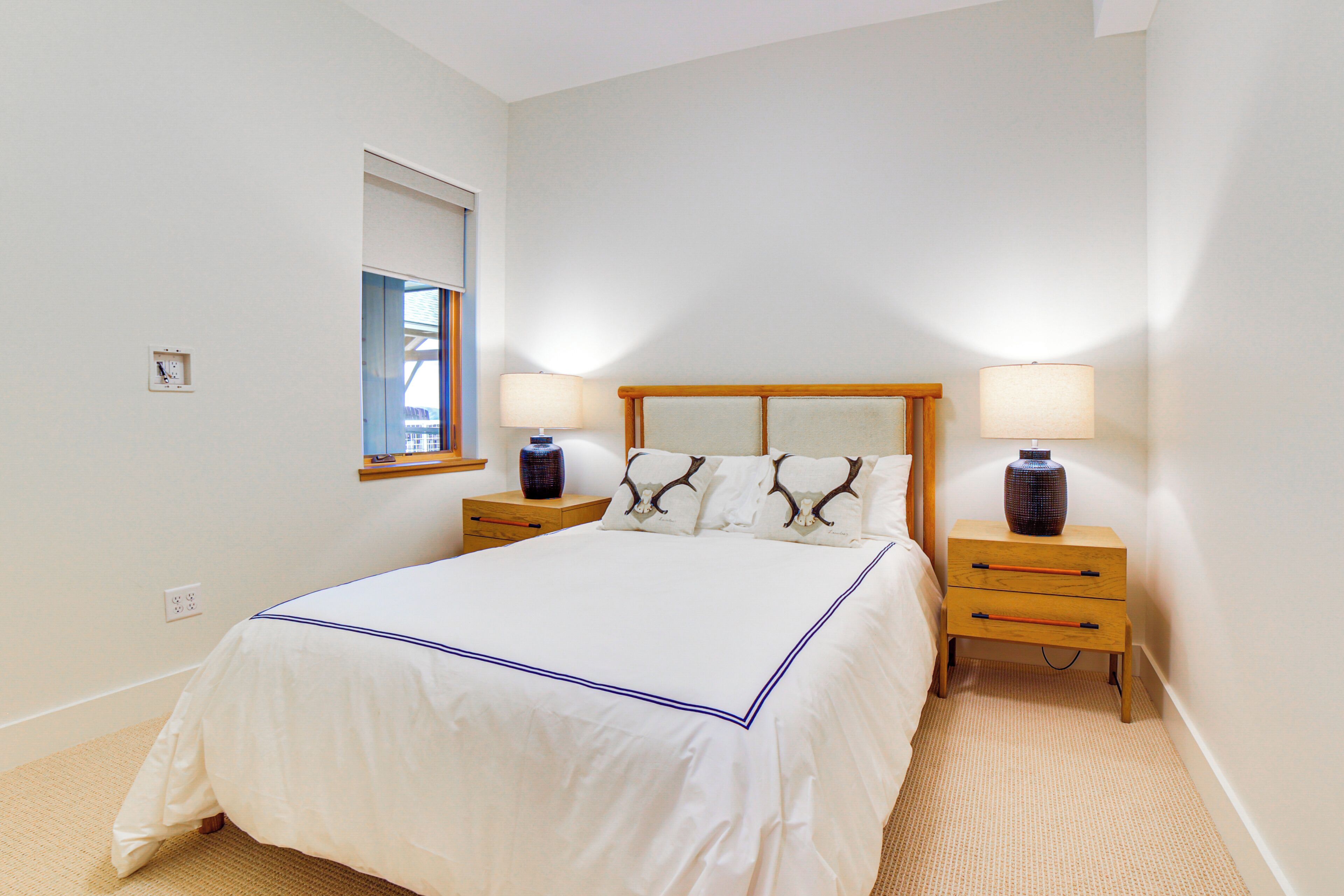A bedroom with a large bed, two bedside tables with lamps, a small window, and a wall clock.